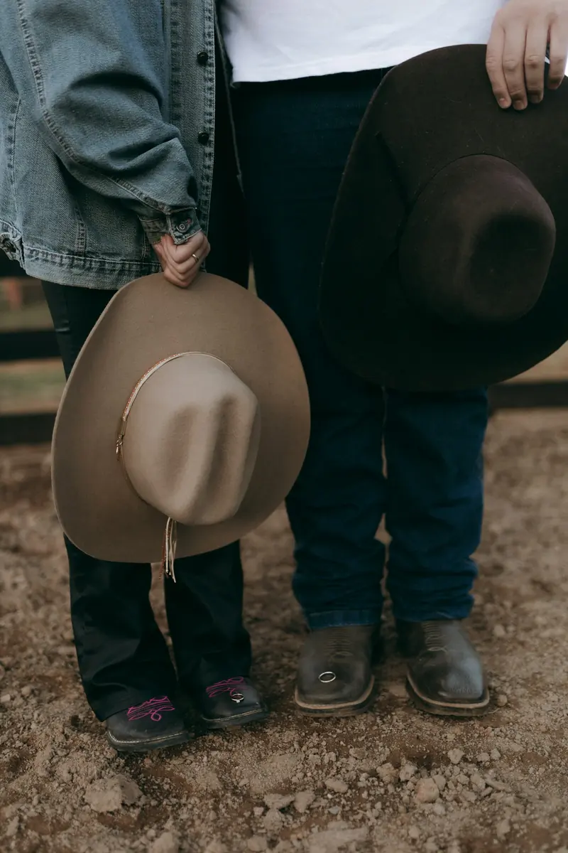 Two people in jeans and boots holding their cowboy hats