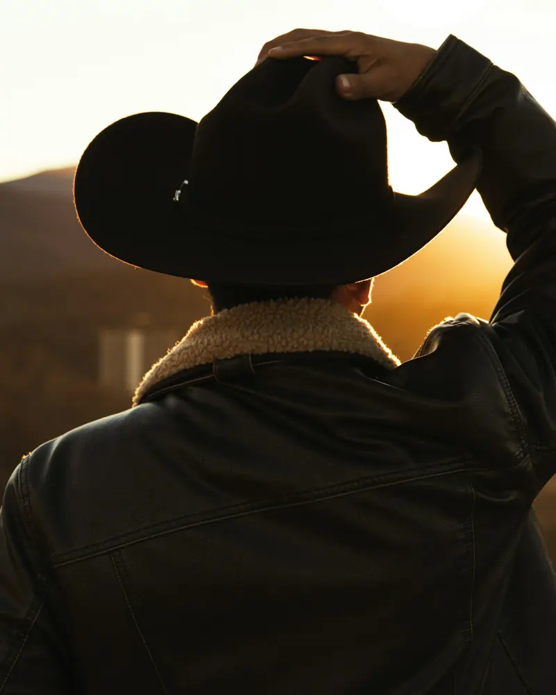 A man setting his black cowboy hat against the evening sun