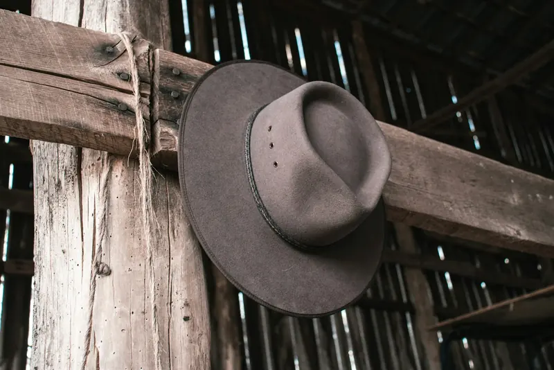 A gray felt cowboy hat hanging on a weathered barn post