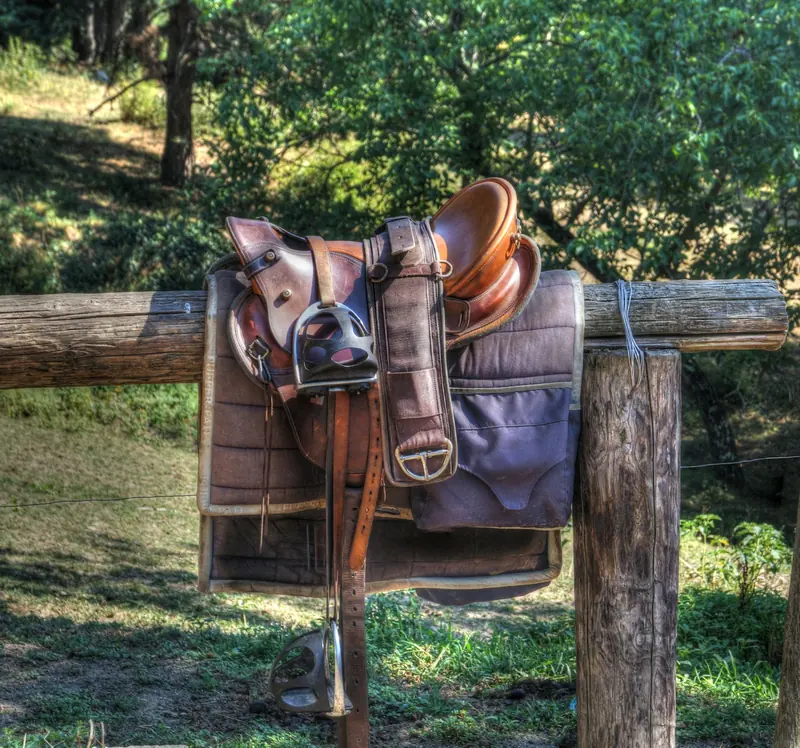A worn saddle resting on a wooden fence rail