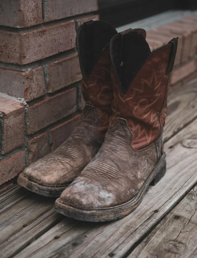 A pair of scuffed brown cowboy boots on a porch