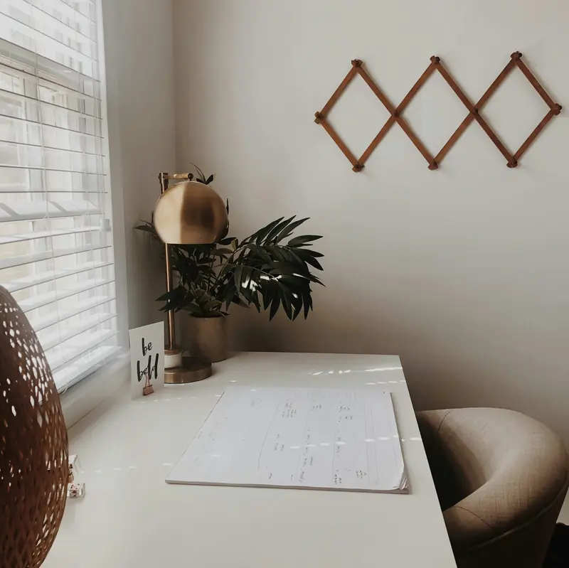 A white desk with a lamp and a plant by a window