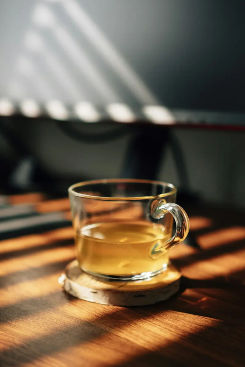 A glass mug of tea on a wood table in the sun