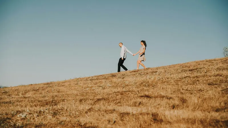A couple holding hands as they walk through a dry grass field