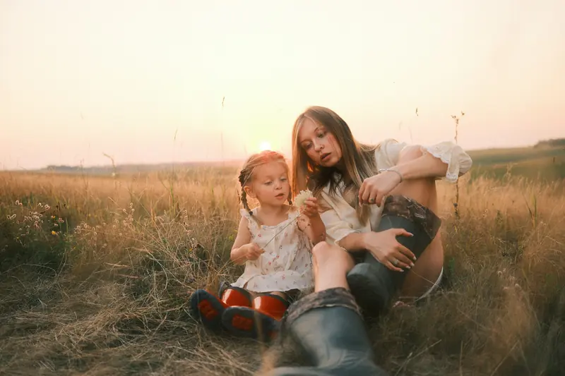 A mother and her little girl sitting in tall grass at golden hour