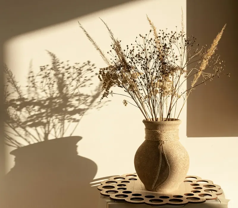 A clay vase of dried flowers in soft window light