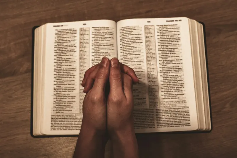 Folded hands resting on an open Bible