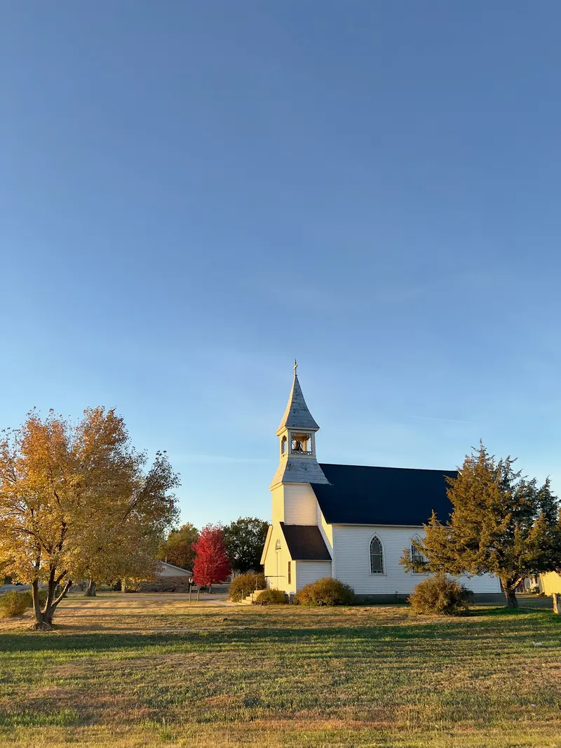 A small white church with a steeple between two fall trees