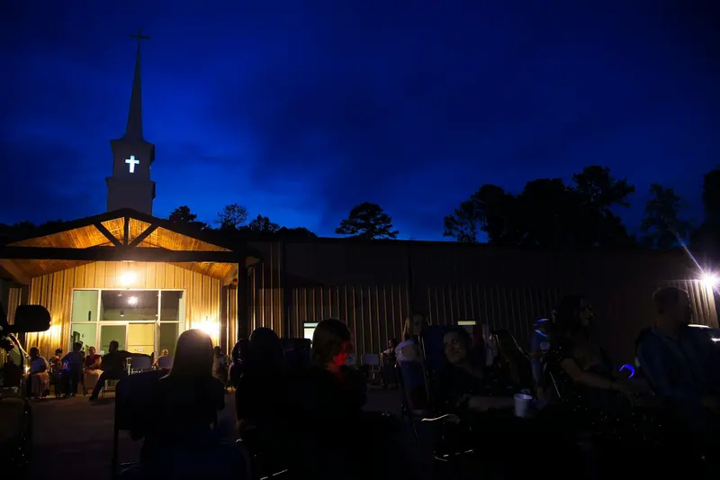 People sitting outside a lit-up church on a summer night