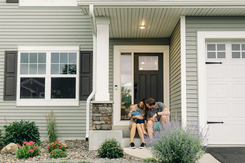 A couple sitting on the front steps of a gray house