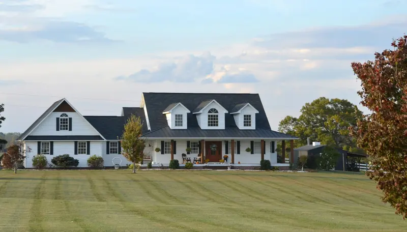 A large white farmhouse with a wraparound porch and a wide lawn