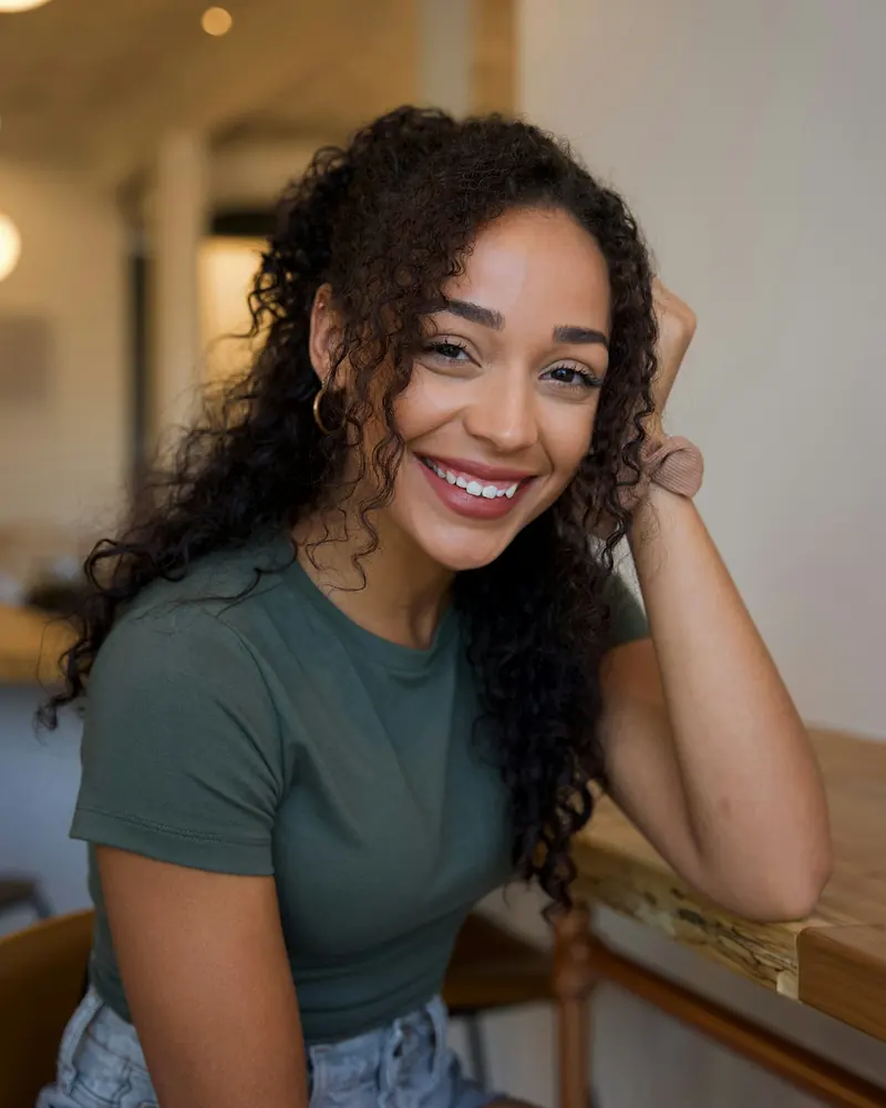 A smiling woman with curly hair sitting at a wooden table