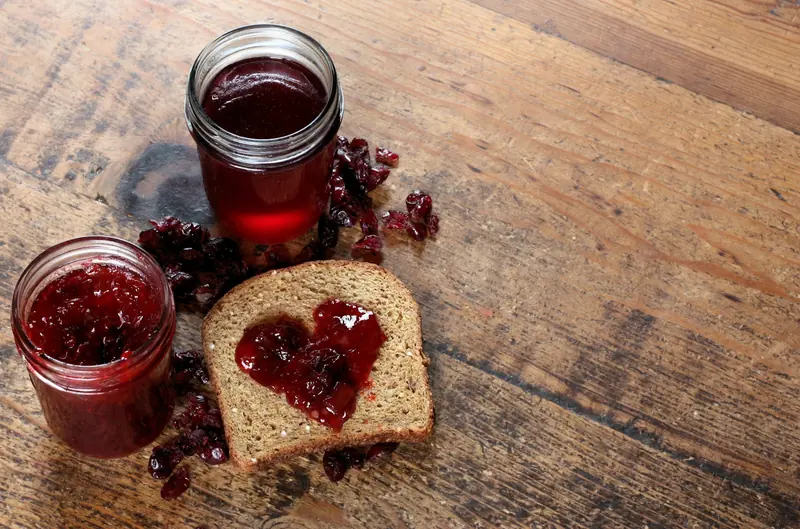 Two jars of jam beside a slice of bread